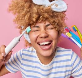 Radosna kobieta trzyma w rękach szczoteczki manualne i szczoteczkę soniczną.