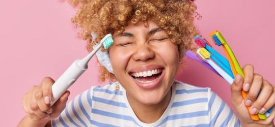 Radosna kobieta trzyma w rękach szczoteczki manualne i szczoteczkę soniczną.
