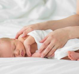 Kobieta przykrywa kocem śpiące niemowlę.