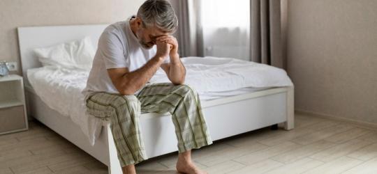 Zmartwiony mężczyzna siedzi na brzegu łóżka, nie radzi sobie z problemem przedwczesnego wytrysku.