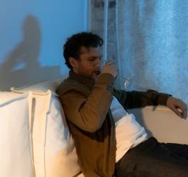 Mężczyzna siedzi na kanapie, pije wino z kieliszka.