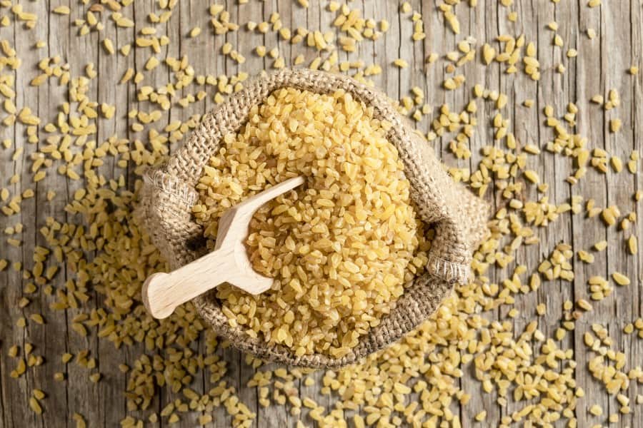 Gruboziarnista kasza bulgur w jutowym worku wraz z drewnianą miarką.