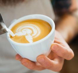 Barista przygotowuje kawę z mlekiem, wykorzystując technikę latte art.