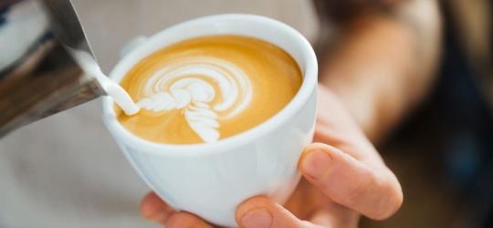 Barista przygotowuje kawę z mlekiem, wykorzystując technikę latte art.