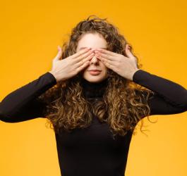 Kobieta w kręconych włosach zasłania dłońmi swoje oczy.