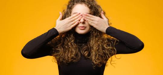 Kobieta w kręconych włosach zasłania dłońmi swoje oczy.
