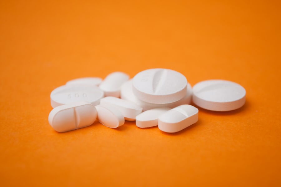 Tabletki zawierające ketoprofen na pomarańczowym tle.