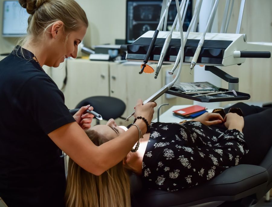 Pacjentka leży na fotelu dentystycznym. Dentystka przeprowadza kontrolę przed ekstrakcją ósemki.