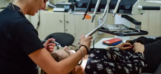 Pacjentka leży na fotelu dentystycznym. Dentystka przeprowadza kontrolę przed ekstrakcją ósemki.