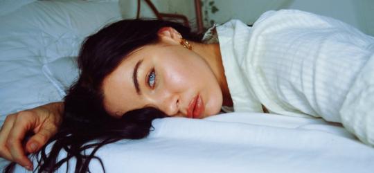 Młoda kobieta leży na łóżku, wygląda na przemęczoną.