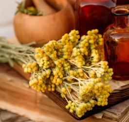 Kocanki piaskowe na drewnianej desce, obok butelki z brązowego szkła i drewniany moździerz..