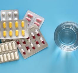 Widok z góry. Szklanka z wodą, obok blistry kolorowych tabletek i kapsułek.