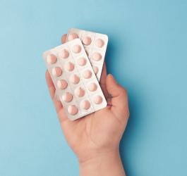 Błękitne tło. Na dłoni dwa blistry z różowymi tabletkami.