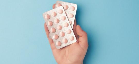 Błękitne tło. Na dłoni dwa blistry z różowymi tabletkami.