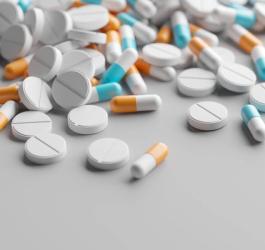 Białe tabletki i kolorowe kapsułki rozsypane na szarym tle.