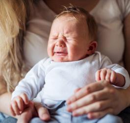 Mama trzyma niemowlę na kolanach. Dziecko ma kolkę niemowlęcą, płacze, jest niespokojne.