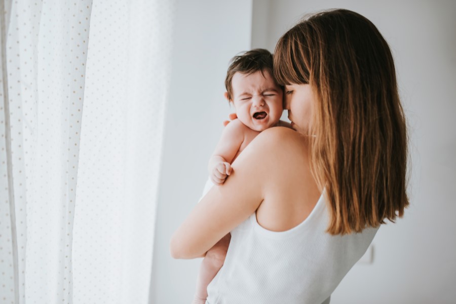 Mama próbuje uspokoić niemowlę, któremu dokucza bolesna kolka.