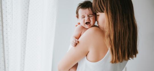 Mama próbuje uspokoić niemowlę, któremu dokucza bolesna kolka.