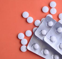 Białe tabletki i blistry na pomarańczowym tle.