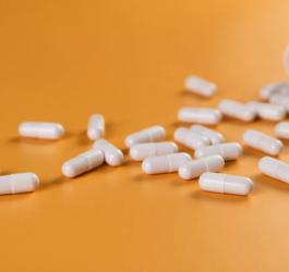Biały kapsułki leku rozsypane na pomarańczowym tle.