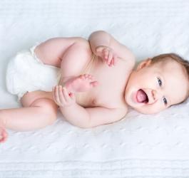Radosne niemowlę leży na białym materacu.