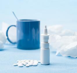 Krople z ksylometazoliną i białe tabletki na błękitnym tle oraz niebieski kubek i chusteczki.