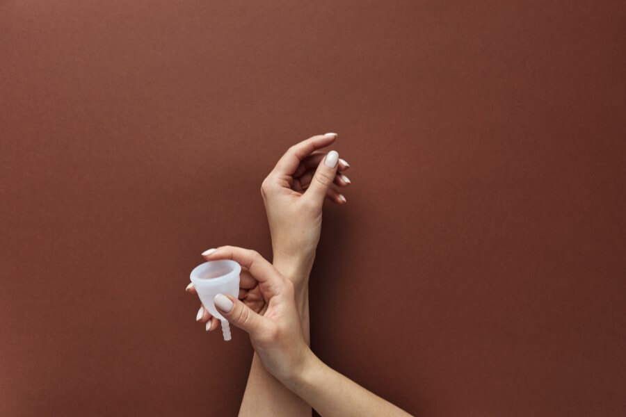 Kobieta trzyma w dłoni kubeczek menstruacyjny.