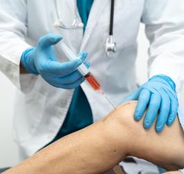 Lekarz wykonuje iniekcję kwasu hialuronowego do stawu kolanowego pacjenta.