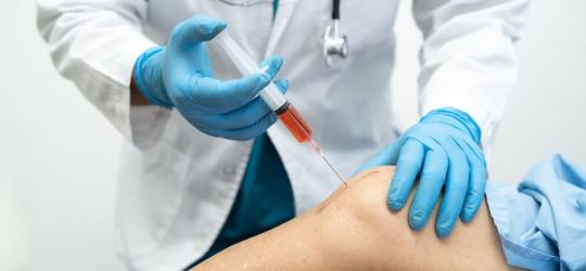 Lekarz wykonuje iniekcję kwasu hialuronowego do stawu kolanowego pacjenta.