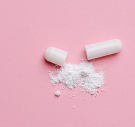 Wysypana zawartość białej kapsułki na różowym tle.