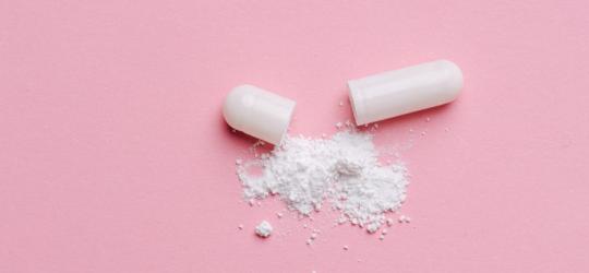 Wysypana zawartość białej kapsułki na różowym tle.