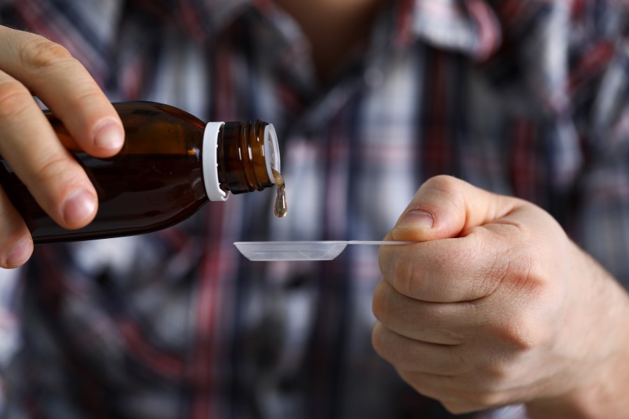 Mężczyzna nalewa porcję leczniczego syropu na łyżeczkę.