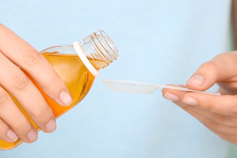 Kobieta nalewa porcję laktulozy na łyżeczkę.