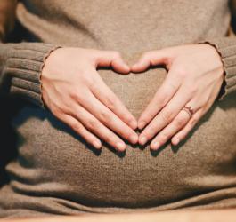 Kobieta trzyma dłonie na ciążowym brzuchu, układa je w kształt serca.