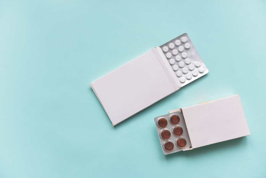 Dwa blistry z białymi i czerwonymi tabletkami na turkusowym tle.