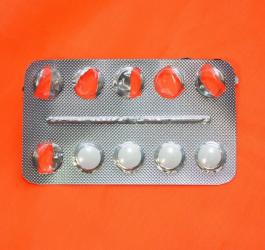 Blister z białymi tabletkami na pomarańczowym tle.