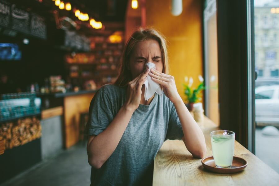 Kobieta w restauracji zmaga się z objawami alergii - katarem i kichaniem.