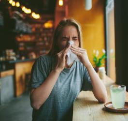 Kobieta w restauracji zmaga się z objawami alergii - katarem i kichaniem.