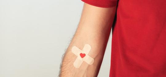 Mężczyzna w czerwonym t-shircie. Na zgięciu łokciowym na naklejony plaster po oddaniu krwi.