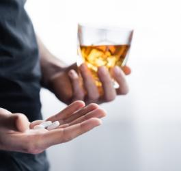 Mężczyzna w jednej ręce trzyma szklankę z alkoholem, w drugiej leki na cukrzycę.