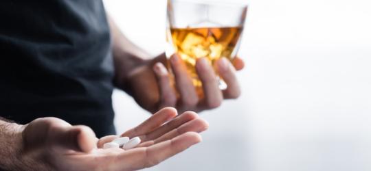 Mężczyzna w jednej ręce trzyma szklankę z alkoholem, w drugiej leki na cukrzycę.