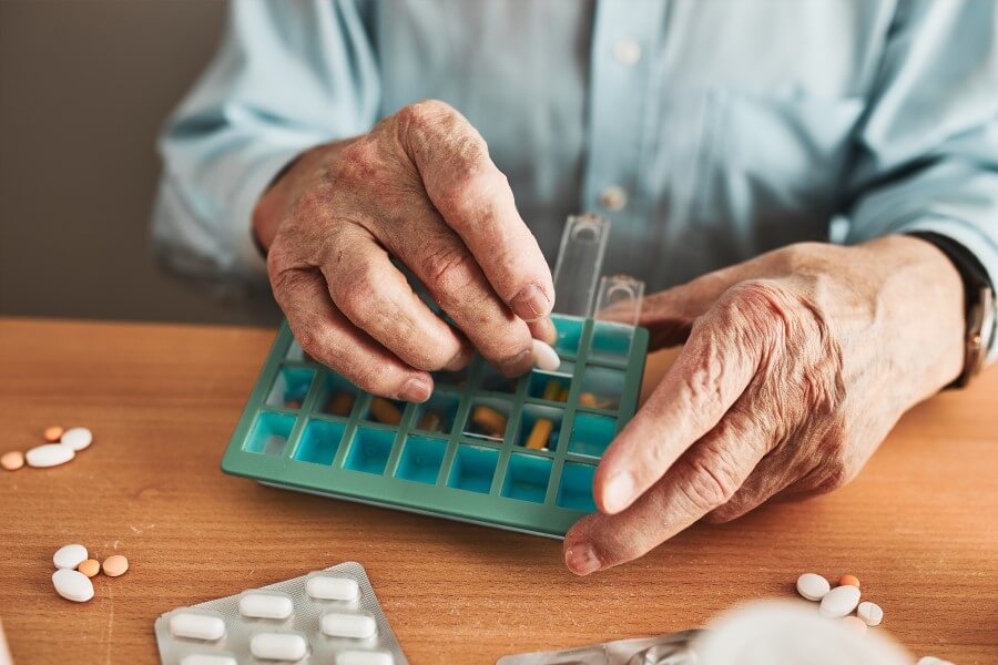 Starszy mężczyzna układa swoje leki w organizerze na lekarstwa.