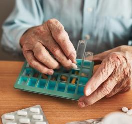 Starszy mężczyzna układa swoje leki w organizerze na lekarstwa.