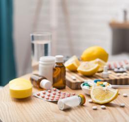 Na stole leżą rozmaite leki na przeziębienie obok cząstek cytryny i szklanki wody.
