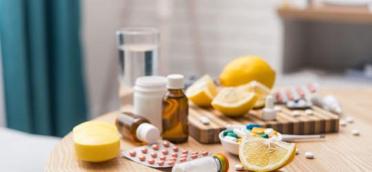 Na stole leżą rozmaite leki na przeziębienie obok cząstek cytryny i szklanki wody.