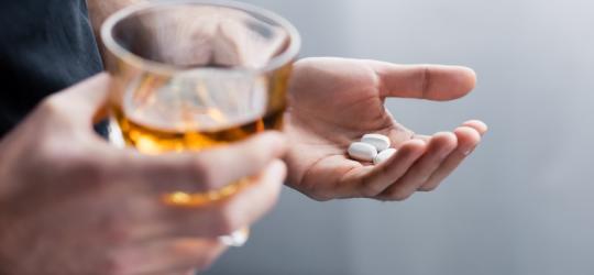 Mężczyzna trzyma w jednej dłoni alkohol w szklance, w drugiej tabletki.