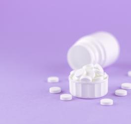 Białe tabletki na fioletowym tle.