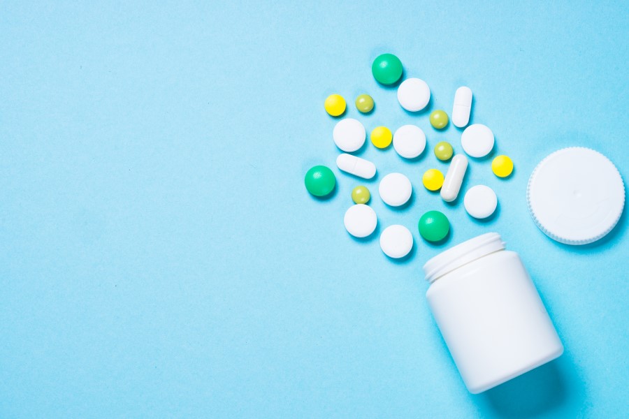 Kolorowe tabletki wysypane z białej fiolki na leki.