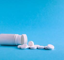 Biała butelka leży na niebieskim tle, obok rozsypane białe tabletki.