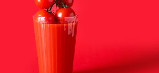 Kiść pomidorów zanurzana w szklance z sokiem pomidorowym – źródłem likopenu.